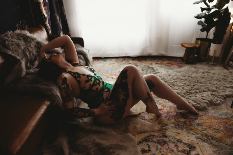 Full body side profile of women in green lingerie with head back on leather couch and left arm up on her head