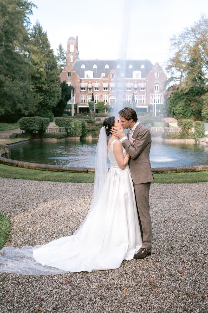 Een koppel wat staat te kussen voor een grote fontein bij Kasteel de Hooge Vuursche