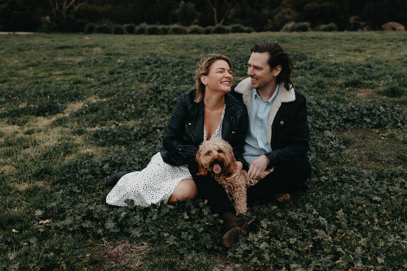 engagement session with dog sitting in the grass laughing