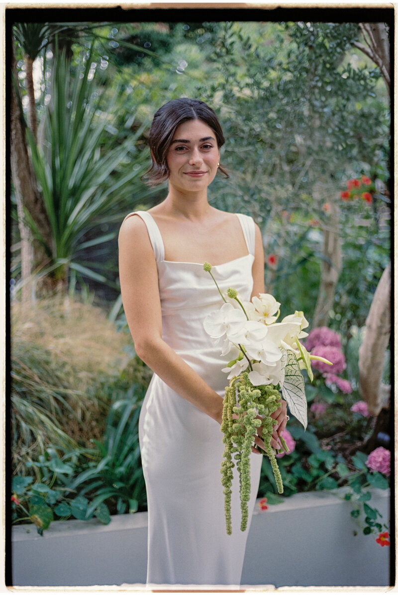 Portrait of bride with cascading orchid bouquet in a garden setting.