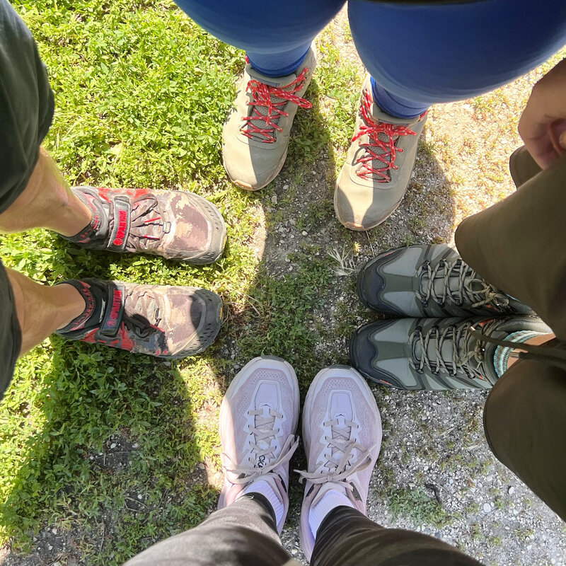 family of 4 looking down at hiking shoes pointed together while hiking
