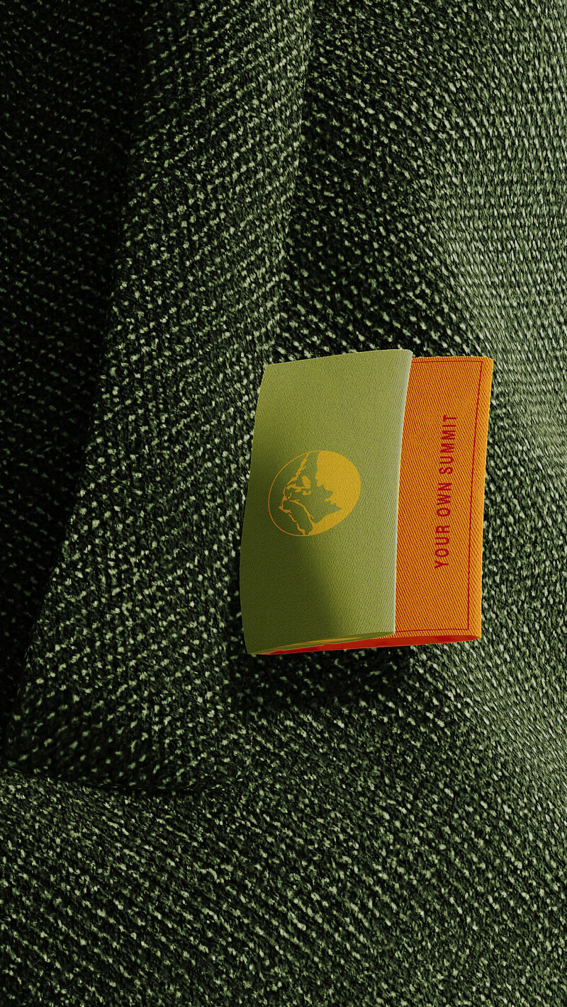 Close-up of Alpath’s woven garment label in green and orange, featuring a mountain emblem and the phrase “Your Own Summit,” reflecting brand identity and timeless outdoor design.