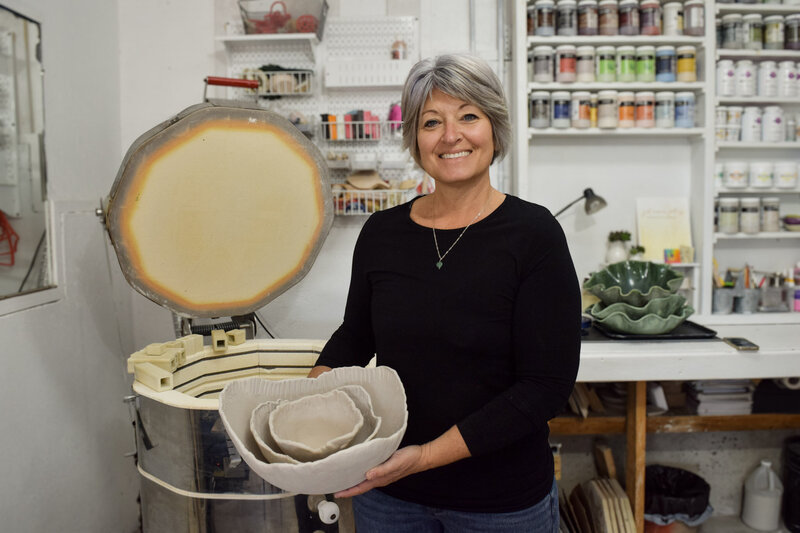 Jill stands beside her kiln inside her Key West, FL and Laingsburg, MI studio holding a set of bisque-fired serving bowls