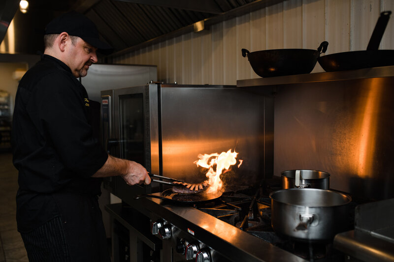 A chef frying rack of lamb over industrial oven.