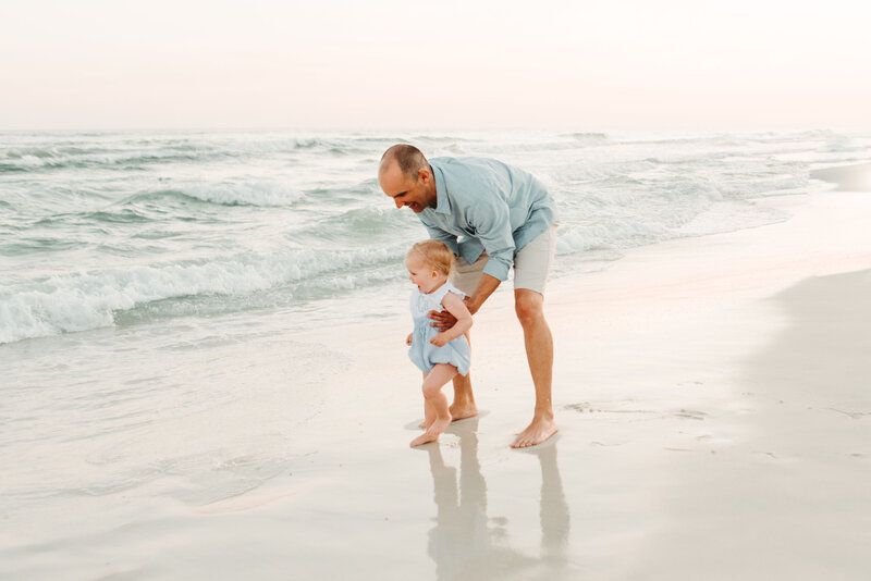 Family Photographer, a young mother and father admire their baby girl at the beach
