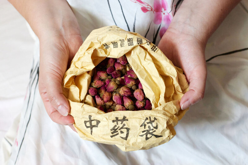 Close up of hands holding a sachet with Chinese characters and dried rose buds in the sachet