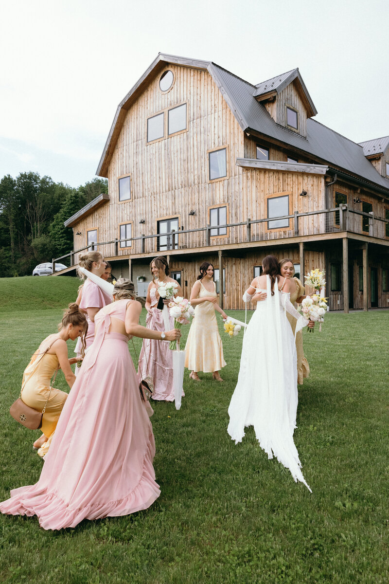 Bride and bridesmaids in flowing dresses celebrating on the lawn in front of the rustic barn venue at Bear Ridge Destination.

