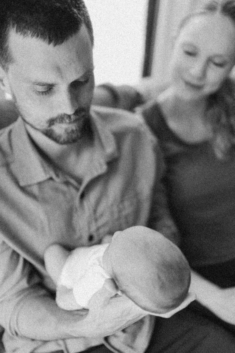 black and white picture of parents holding newborn on couch