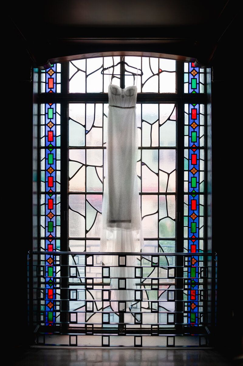 Wedding dress hangs on a stained glass window