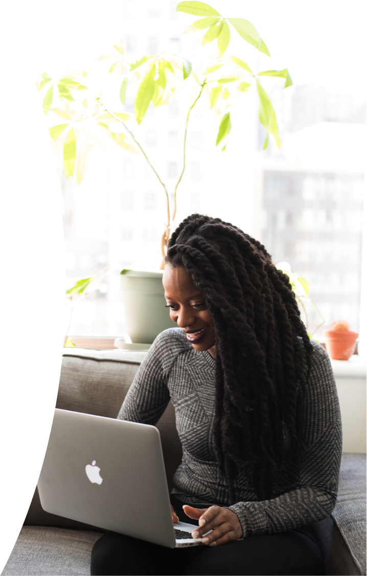 Woman smiling while writing in a notebook outdoors, wearing earbuds and working beside a laptop.