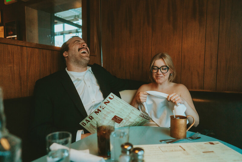 While in a diner in Denver, Bride and groom laughing while ordering dinner at the end of their Colorado elopement.