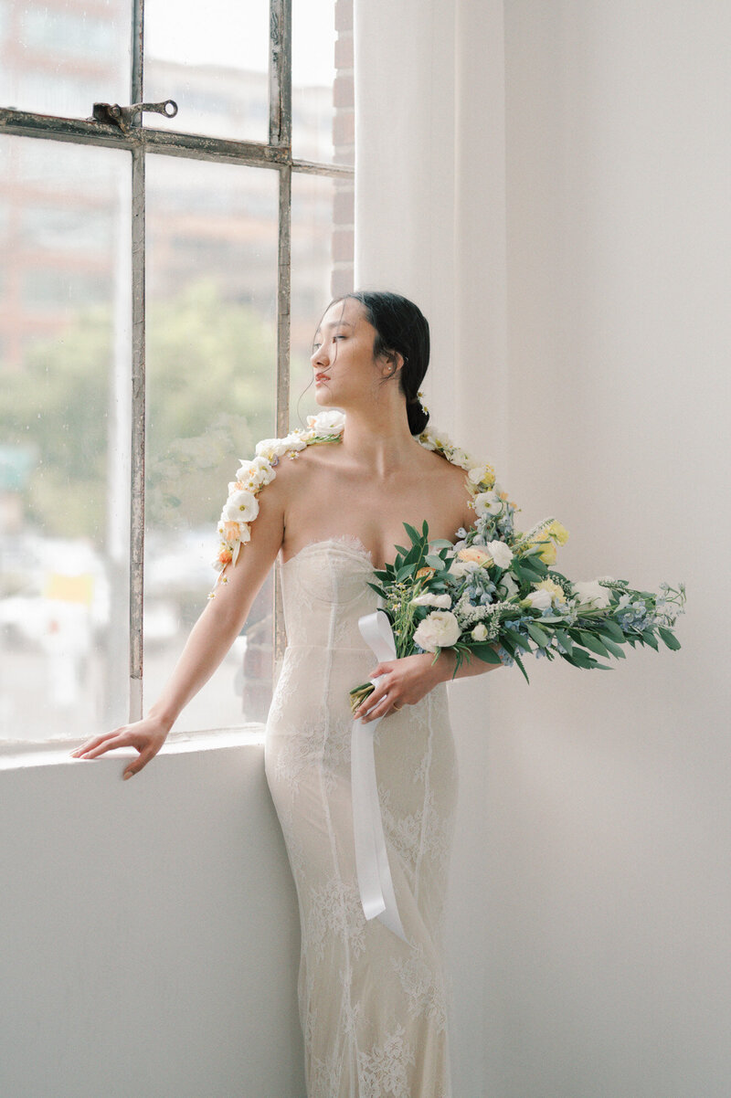 Bride looking out window holding wedding flowers