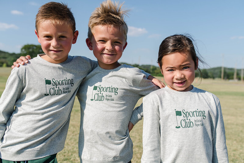 Three little kids smiling and wearing Sporting Club sweatshirts