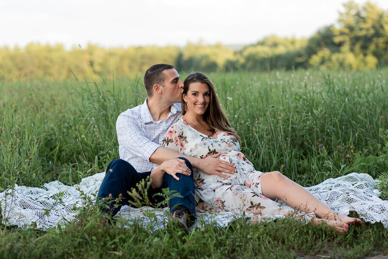 Couple in field, looking down at pregnant mom's belly