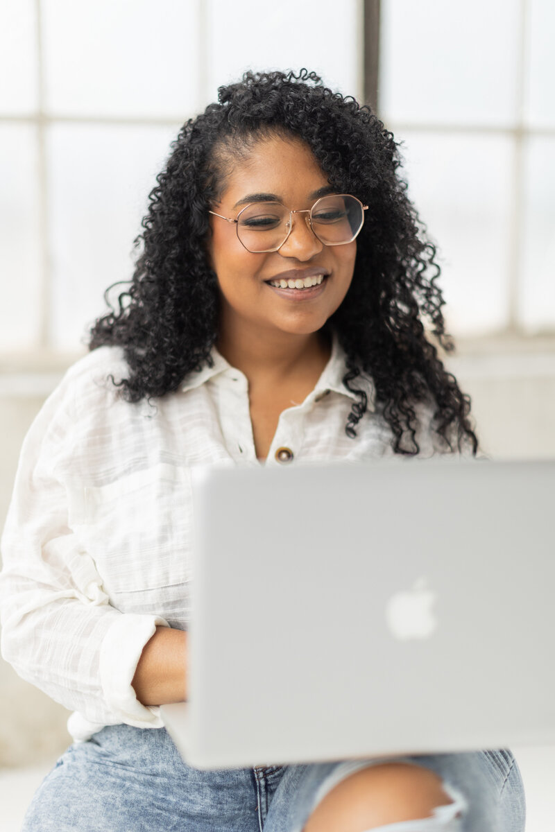 Alexa Luckenbach, smiling while working on her laptop, providing strategic website design for female service-based business owners