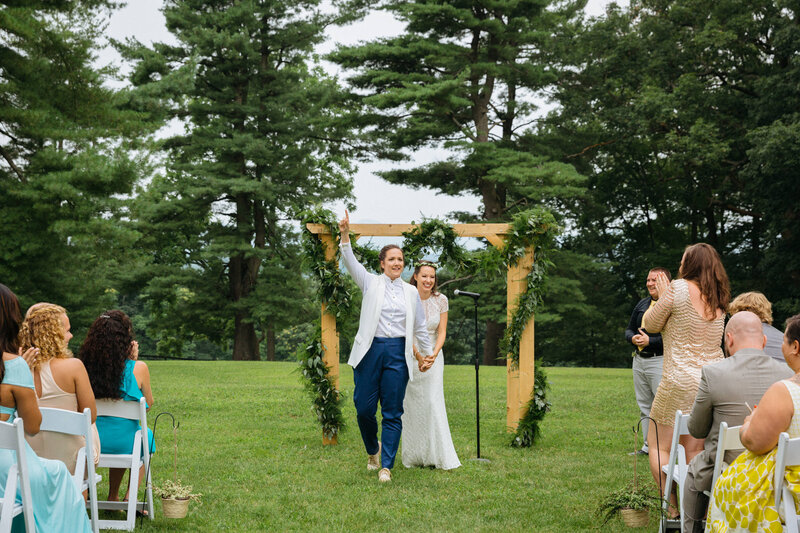 A married couple walking up the aisle after their ceremony while one holds their hand up.