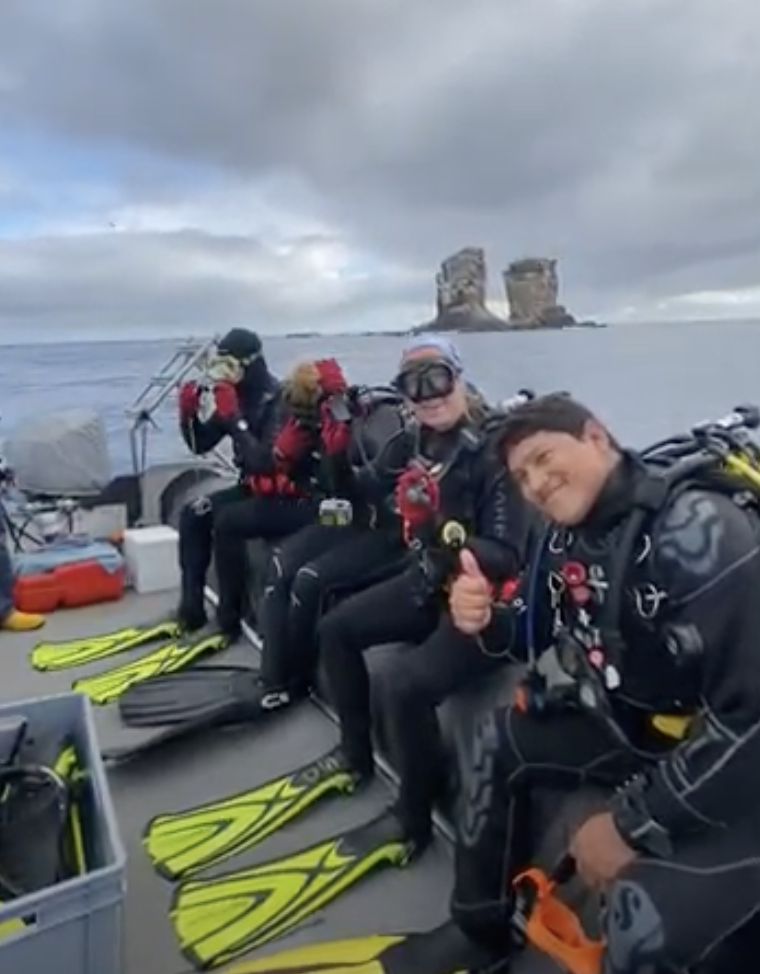 Scuba divers giving thumbs up in full gear and wet suits sitting on the edge of the boat