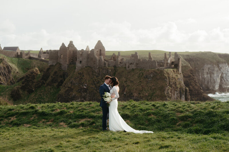Elopement Photo Ideas | Eloping couple hugs each other on an ocean cliff with an ancient castle ruin in the background