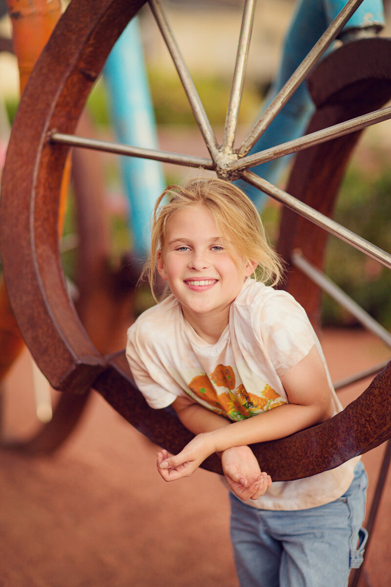 Tween girl is playing in Carmel on some oversized bicycles, smiling at the camera.