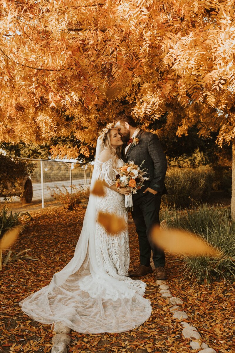 bridal couple embracing in fall trees with leaves falling