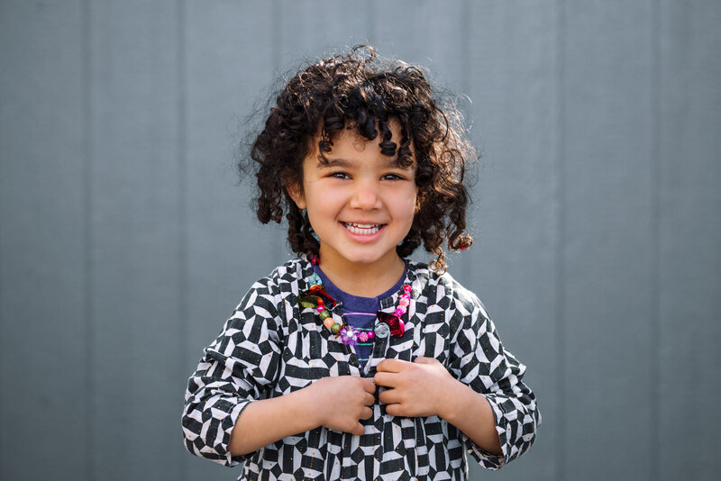 preschool girl with color outfit and accessories smiling and looking at the camera during a school portrait at her Oakland preschool