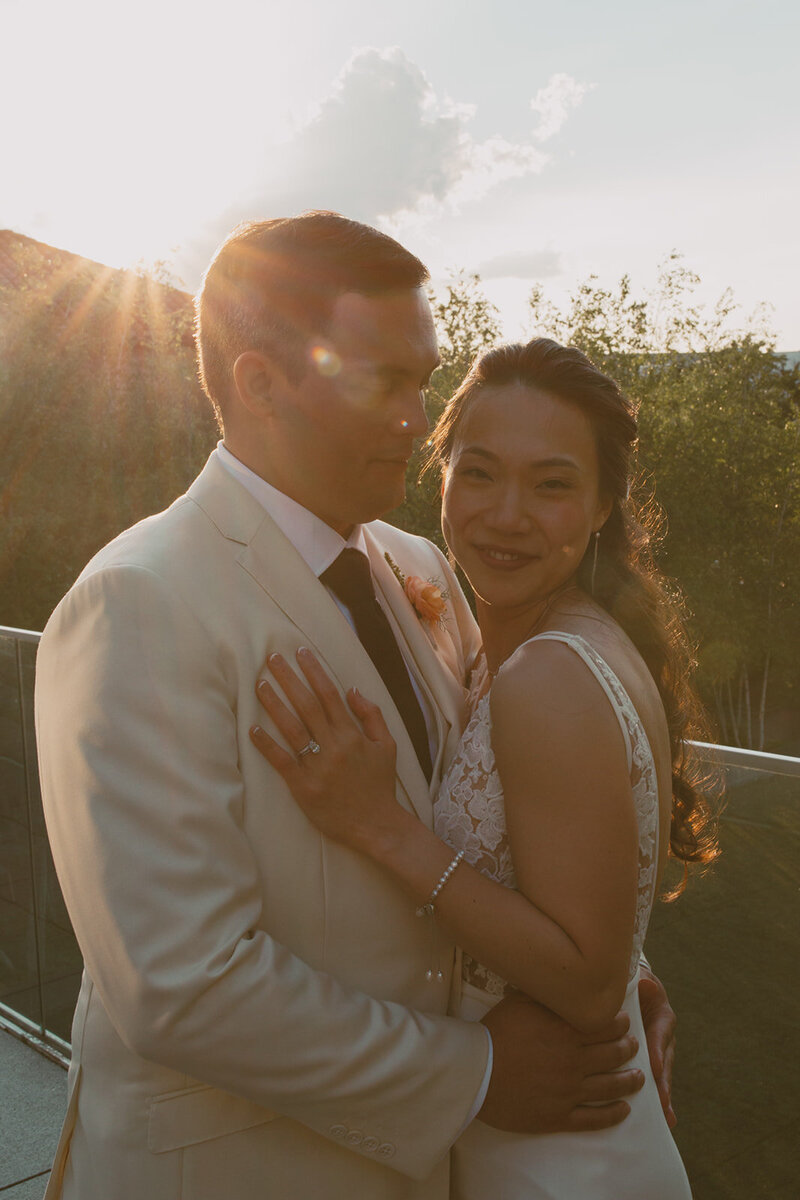 bride and groom pose on a bench in front of rose bush
