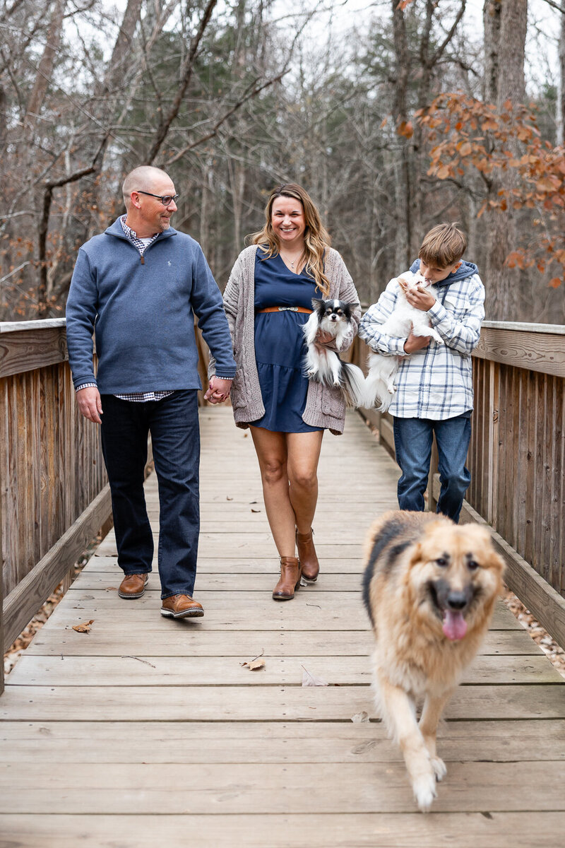 Family walking on a wooden bridge with dogs during an outdoor portrait session in Farmington, Missouri. 