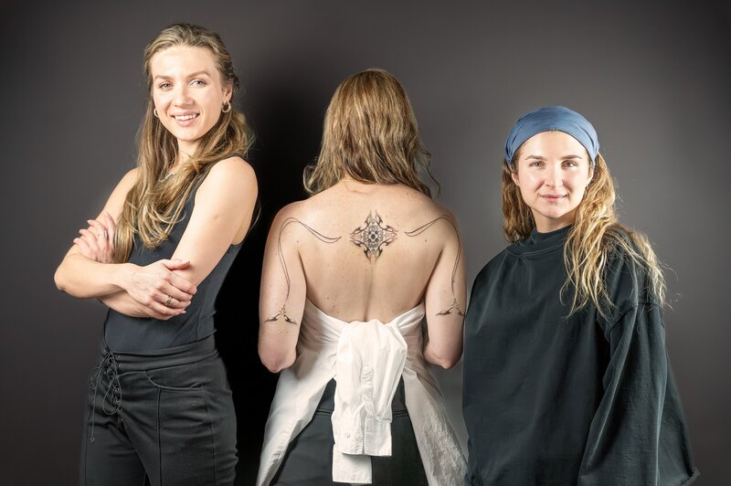 Two sister tattoo artists standing next to their client's completed artwork