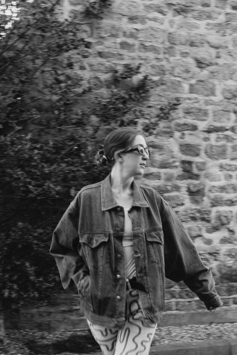 Black and white image of stylish business coach on a walk in Oxfordshire against Cotswold stone