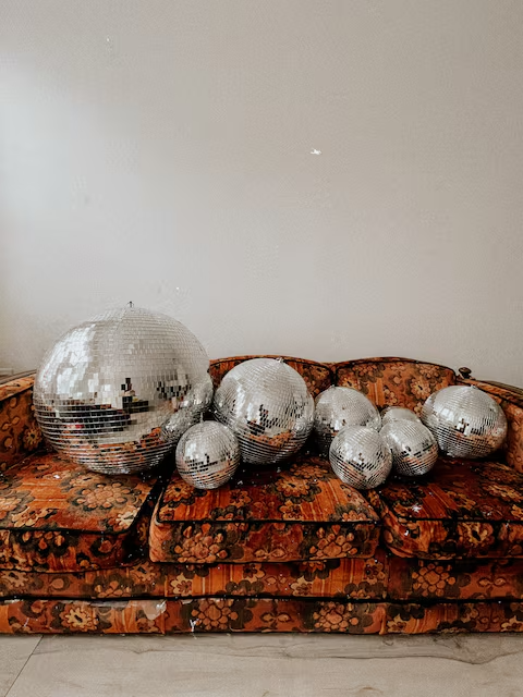 A lineup of disco balls on a floral vintage sofa sets the tone for your retro stay at Groovy Shack, close to Carillon Beach and Santa Rosa.