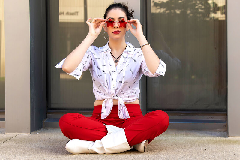 Senior girl in white printed top, red pants, white boots, red sunglasses sitting causually