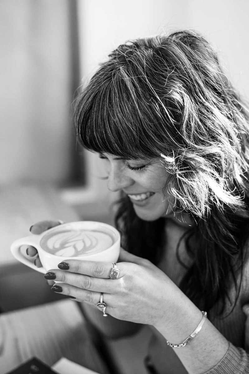 A woman holds a latte and smiles, representing an example of work by branding and lifestyle photographer Among the Oaks. 