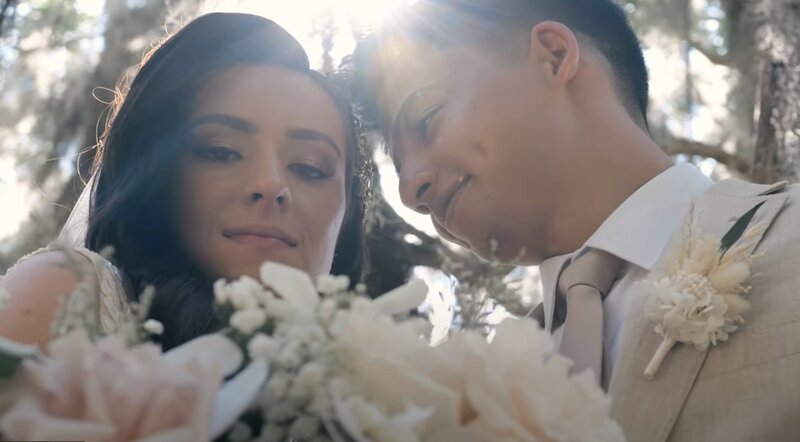 A newlywed couple standing close with the sun shining behind them 