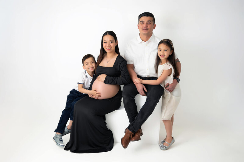 Expecting mother surrounded by her partner and two children, all embracing in a loving hug.