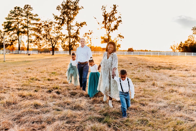 a family of five playing follow the leader in a field during golden hour