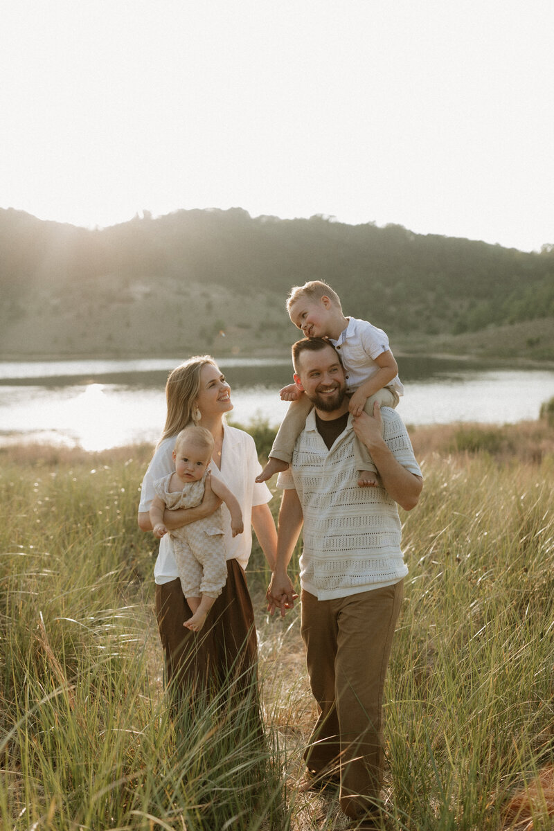 Stephen and Kaity from Rainstorm Photo & Video walking through tall grass with their two children at sunset, photographed in a candid, heartfelt style.