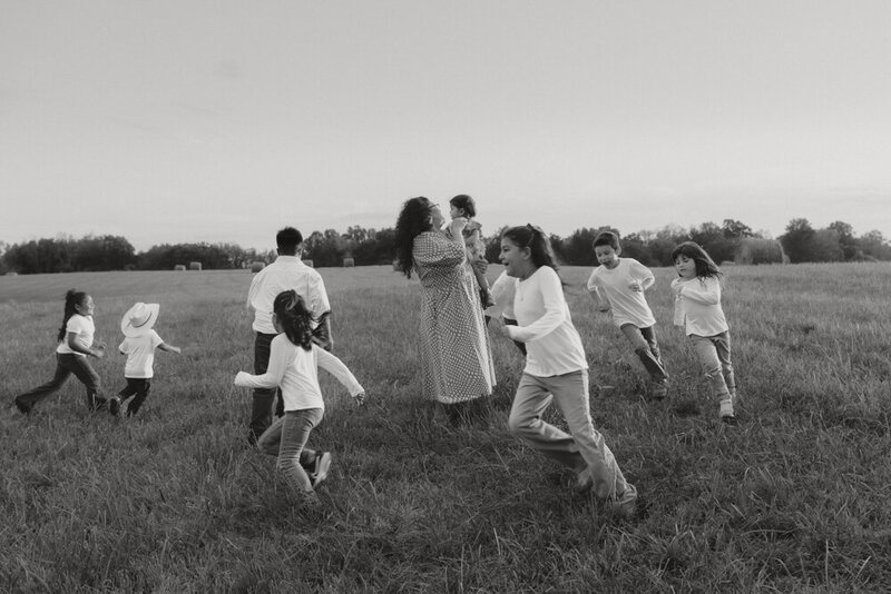 A family session in Jonesborough, TN at Forty Acres Farm. A grandmother stands holding her youngest grandchild while the rest of her grandchildren run around her. Northeast, TN Lifestyle Family Photographer. 