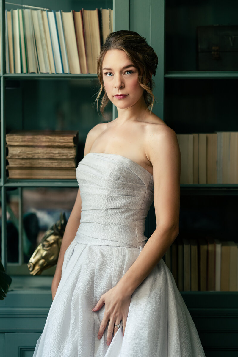 A bride wearing a grey wedding dress stands in front of an antique bookshelf