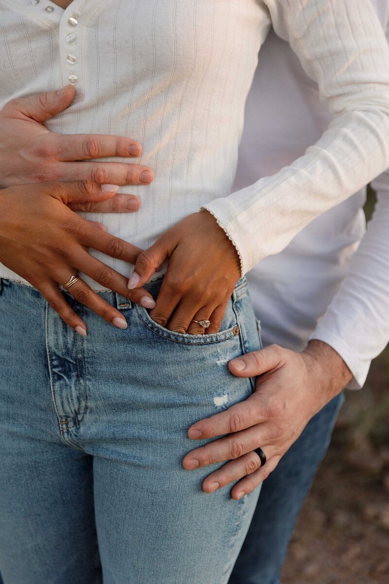 Boyfriend intimately hugs his fiancé from behind and holds her hands.