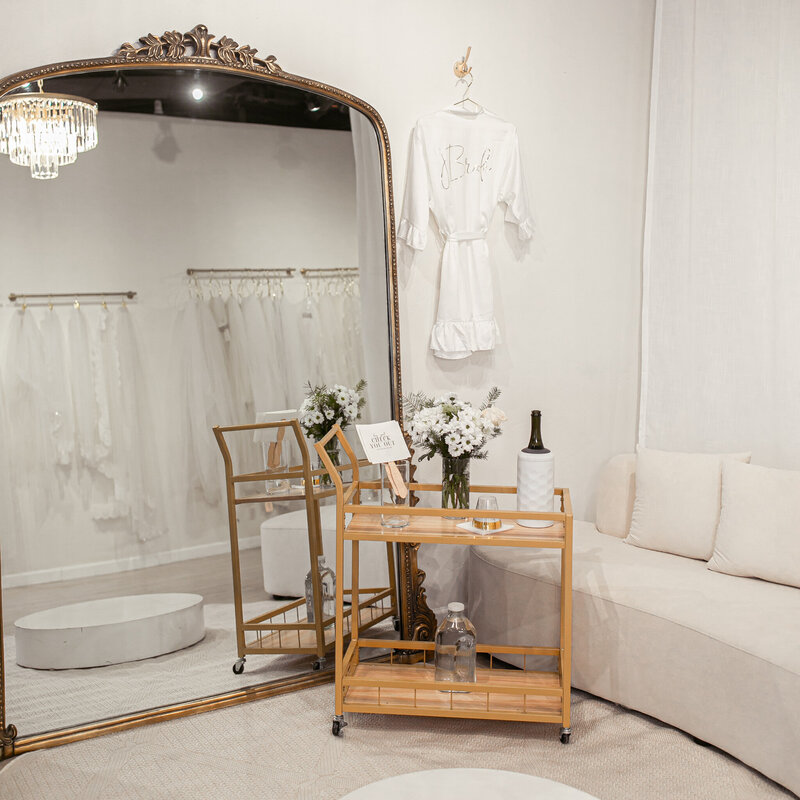 Bridal Bliss Experience setup in front of a large mirror and stage at our semi private lounge. Bridal robe, and a cart with flowers and champagne.  