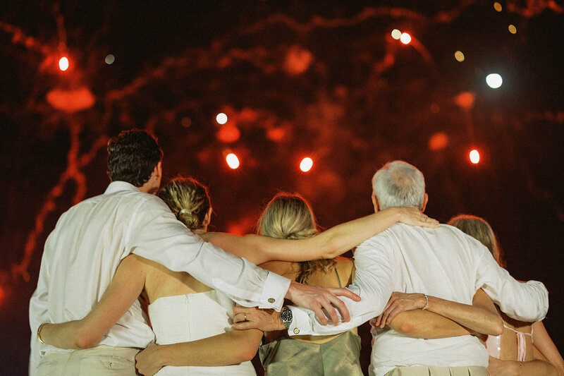 A family sharing a loving embrace under a sky filled with fireworks during their oldest daughter destination wedding celebration at Casa Colonial Beach & Spa— photographed by Asia Pimentel Photography.