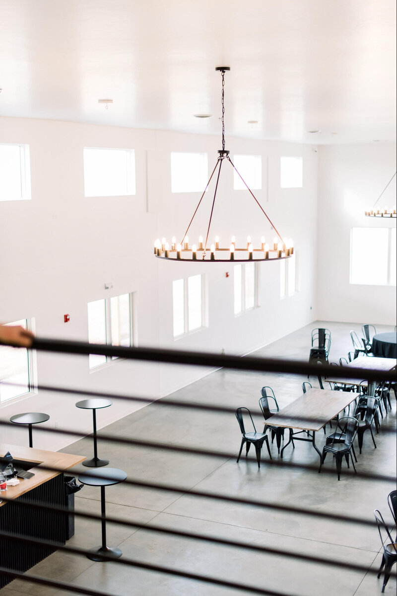 Interior of the August House venue in Dickinson, North Dakota, showing a spacious white-walled wedding reception hall with high ceilings, large windows, minimalist decor, and modern chandelier lighting.