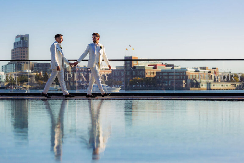 A couple holds hands while walking along the edge of a pool overlooking downtown Baltimore