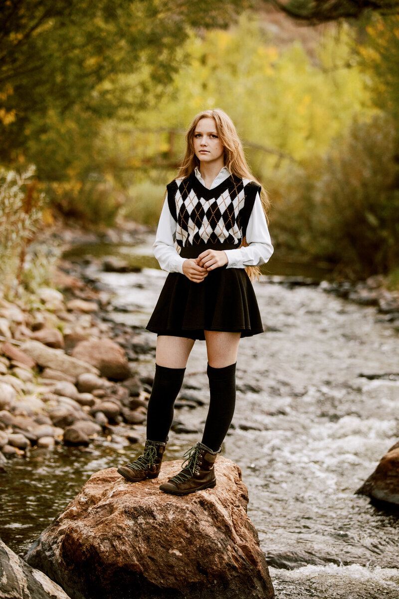 girl in vest and skirt stands on a rock in a river