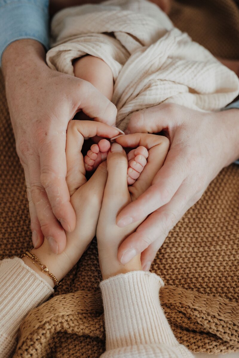 Mann und Frau formen mit ihren Händen ein Herz um die Füße des Babys