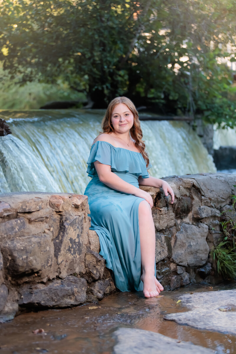 Fuquay Varina High School Senior sitting on a rock wall by a waterfall in Raleigh, NC.