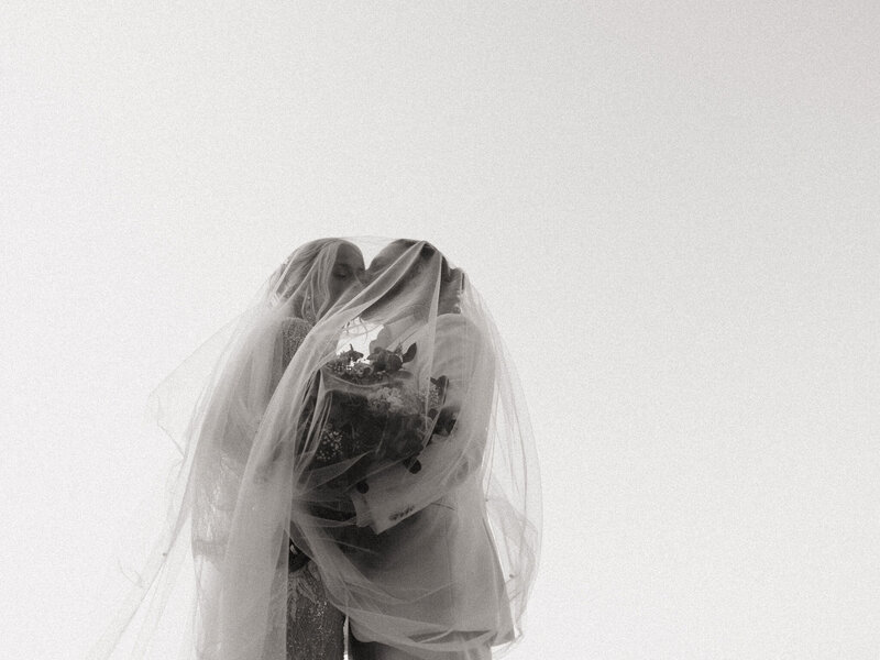 black and white photo of bride and groom with the brides veil over both of them