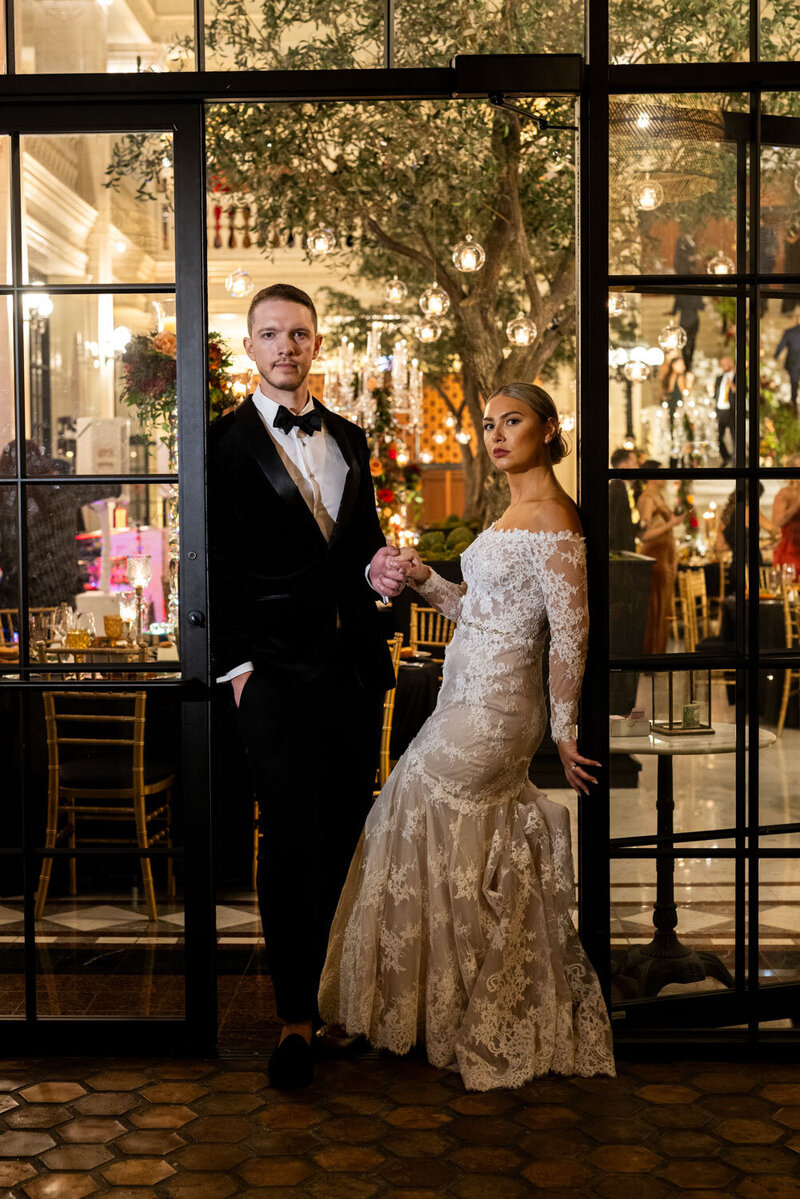 A bride and groom are posing for a picture in front of a glass door.