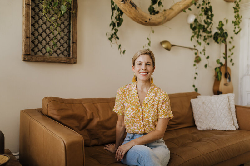 Lela Tuhtan sitting on a brown couch in a yellow shirt.