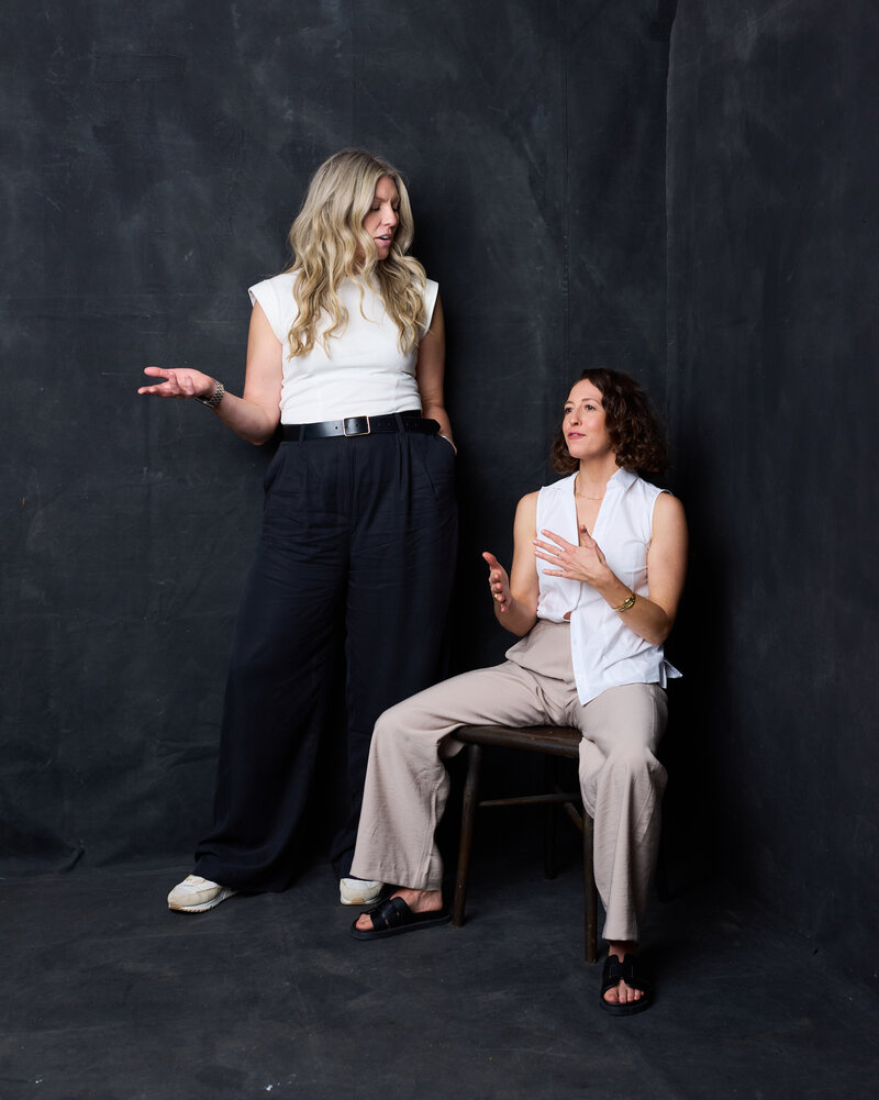 Two female strategists in a conversation/consultation pose against a dark studio backdrop